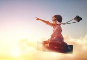 Child using imagination to travel on briefcase with helmet, goggles, and camera