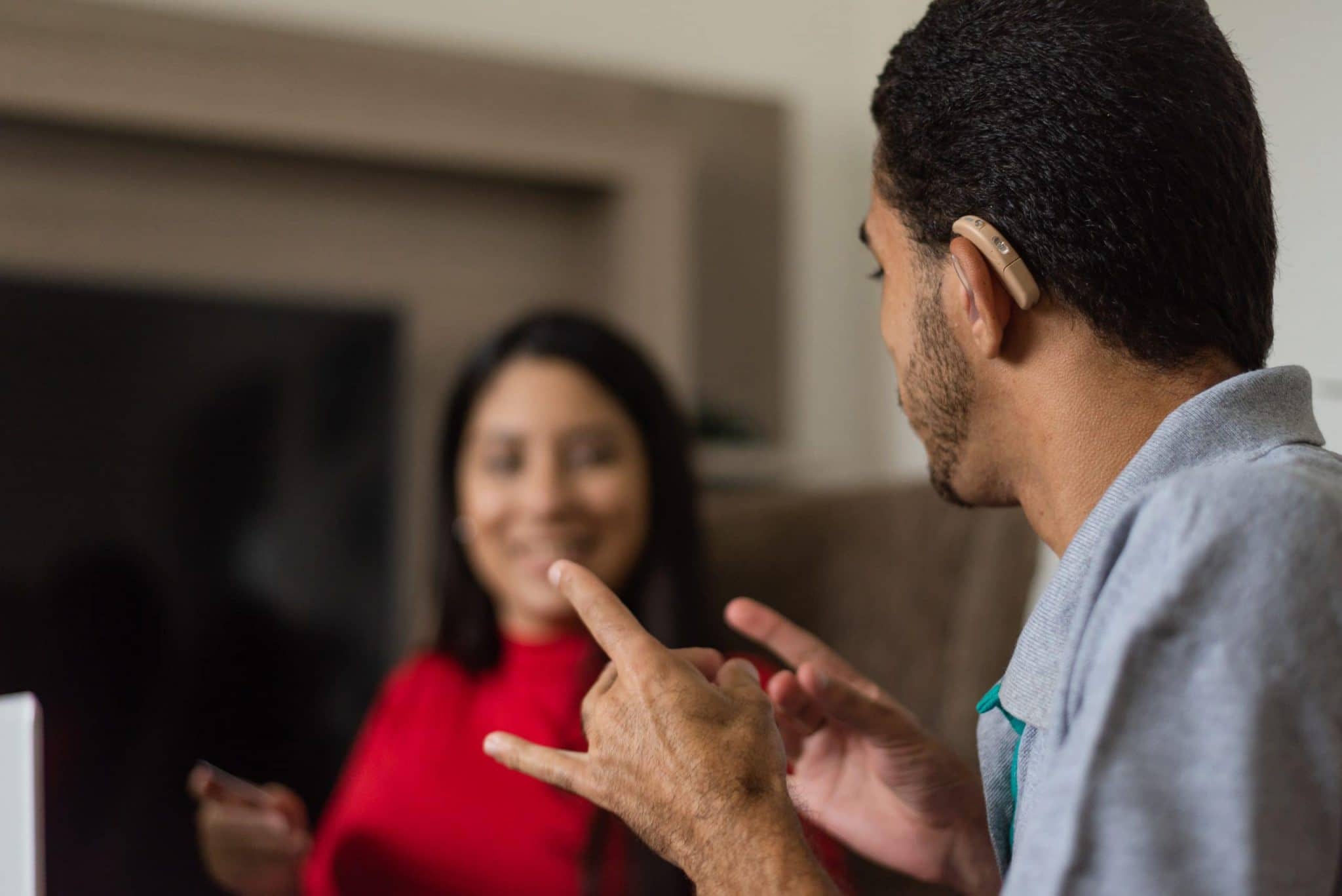 Hard of hearing man, wearing hearing aides, using sign language to communicate with woman in red dress.