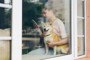 A picture of a women with her dog; she is looking at her phone and using headphones.